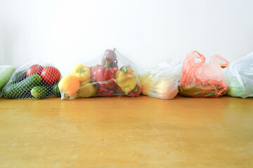 Plastic bags with groceries compared to eco mesh produce packaging with vegetables on wooden table....