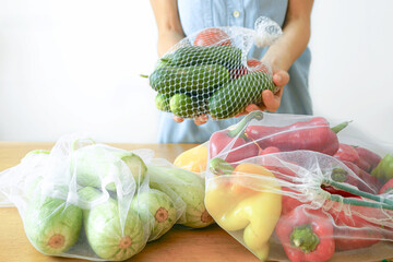 Woman holding fresh vegetables in reusable mesh produce bag demonstrating zero waste shopping. Sustainable grocery storage and green habits. Eco-friendly lifestyle and plastic-free kitchen concept