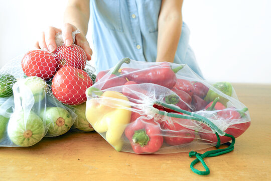 Woman unpacks colorful vegetables from eco mesh bags. Zero plastic lifestyle with reusable produce bags and fresh organic food. Eco shopping, healthy seasonal diet and conscious consumption concept