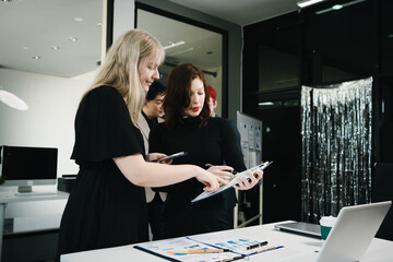 Four colleagues engage in a collaborative office meeting, using laptops, tablets, and documents to brainstorm ideas, discuss strategies,share insights, fostering teamwork, productivity, professional