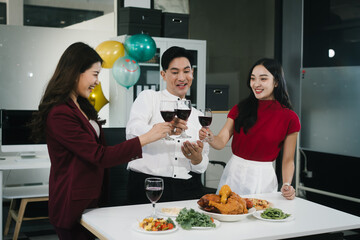 Four cheerful friends celebrate together in an office party, enjoying delicious food, fried chicken, pizza, salad, wine. Surrounded by balloons and laughter, they share happiness, marking   year-end