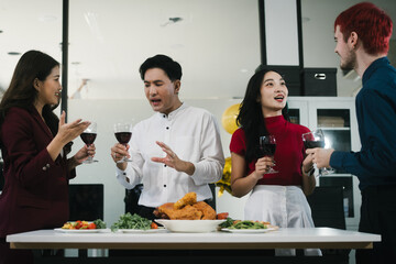 Four cheerful friends celebrate together in an office party, enjoying delicious food, fried chicken, pizza, salad, wine. Surrounded by balloons and laughter, they share happiness, marking   year-end