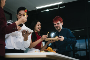 Four cheerful friends celebrate together in an office party, enjoying delicious food, fried chicken, pizza, salad, wine. Surrounded by balloons and laughter, they share happiness, marking   year-end
