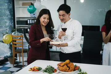 Four cheerful friends celebrate together in an office party, enjoying delicious food, fried chicken, pizza, salad, wine. Surrounded by balloons and laughter, they share happiness, marking   year-end