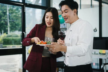 Four cheerful friends celebrate together in an office party, enjoying delicious food, fried chicken, pizza, salad, wine. Surrounded by balloons and laughter, they share happiness, marking   year-end