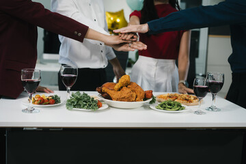 Four cheerful friends celebrate together in an office party, enjoying delicious food, fried chicken, pizza, salad, wine. Surrounded by balloons and laughter, they share happiness, marking   year-end