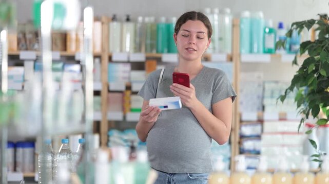 Attentive pregnant woman buyer scanning qr code for box of ointment or gel in small pharmacy