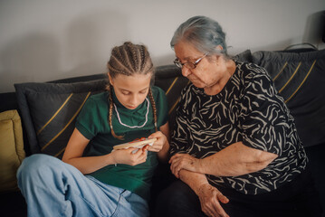 Grandmother teaching granddaughter cross-stitch embroidery on sofa