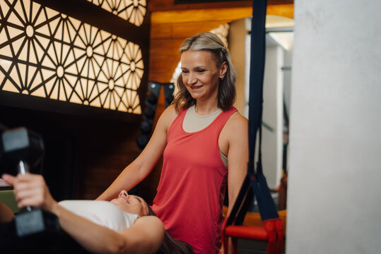 Personal trainer supporting woman lifting weights in gym - Powered by Adobe