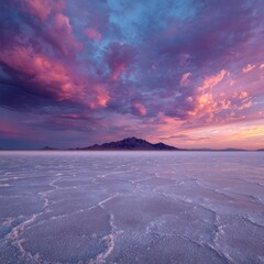 Vibrant sunset hues paint a dramatic sky above a vast, cracked salt flat; a distant mountain silhouetted against the fiery clouds