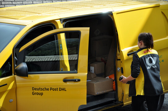 Deutsche Post DHL Group: gelbes Postauto mit Paketen und Personal bei der Auslieferung.