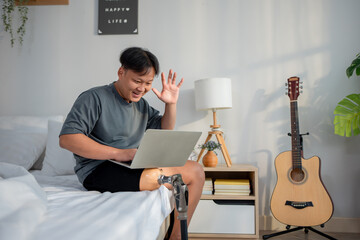 Asian man with prosthetic doing virtual video call on laptop in house. 