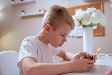 A boy with hearing aids engages with a smartphone, playing mobile games with focused enjoyment....
