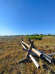 Low-angle view of metal pipe structure on dry grassy field under clear blue sky. Ideal for military, outdoor, rural, or environmental contrast-themed visual content