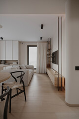 Cozy living room with natural light, soft colors, and a TV mounted on a sleek wooden media unit. Modern design featuring a stylish sofa and shelving.