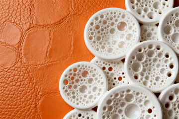 White circular objects with perforated patterns arranged on an orange textured surface