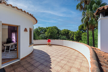 A sunny terrace overlooking the forest, with a single red chair and an open door to the room.