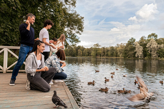 Parents with children at a pond feeding ducks near a lake in a park.