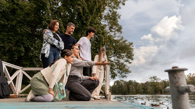 Parents with children at a pond feeding ducks near a lake in a park.