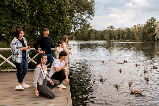 Parents with children at a pond feeding ducks near a lake in a park.