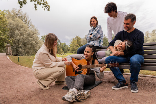 multigenerational group of friends plays guitar and sings by the lake.