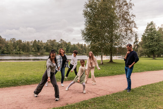 group of people imitate dance moves after a little girl in a park.