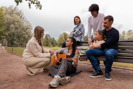 multigenerational group of friends plays guitar and sings by the lake.