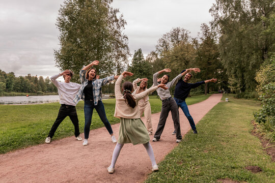 group of people imitate dance moves after a little girl in a park.