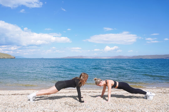 Friends engage in training exercises on the beach under a clear blue sky at midday
