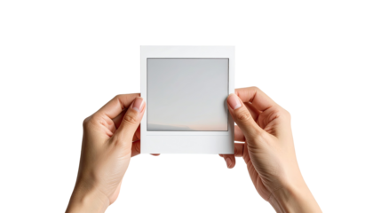 Close-up of hands holding a blank instant photo frame.  Pale, light-grayish  background visible through the frame.  Soft, natural light