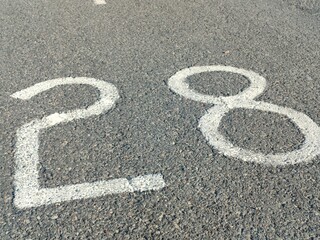 Close-up of number “28” painted in white on textured asphalt. Ideal for signage, race track, parking zone, or urban infrastructure-themed visual content