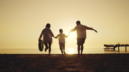 Little boy holding hands on mom and dad, family running together to ocean. Silhouette of people on sandy beach, parents and child feeling happiness and joy, rear view, amazing sunset or sunrise - Powered by Adobe