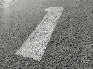 Close-up of a white directional arrow painted on textured asphalt, pointing forward. Ideal for traffic, signage, urban design, or transportation-themed visual content