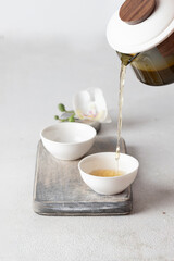 Pouringherbal tea into handcrafted cups, minimalist table setting with soft colors and natural...