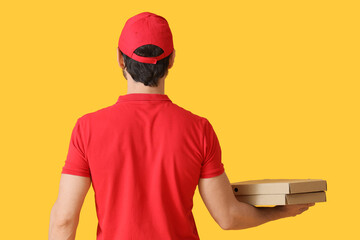 Male courier with pizza boxes on yellow background, back view