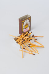 An open matchbox with numerous wooden matches scattered around and inside, set against a clean white background.