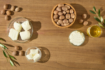 Top-down photo of raw shea butter, shea nuts, and oil, arranged in lab glassware on wooden table. Perfect for background or branding use.