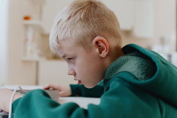 A boy with hearing aids focuses intently while playing a game on his laptop, showcasing modern...