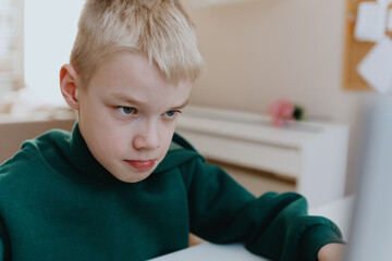 A boy with hearing aids focuses intently while playing a game on his laptop, showcasing modern...