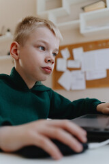 A boy with hearing aids focuses intently while playing a game on his laptop, showcasing modern...