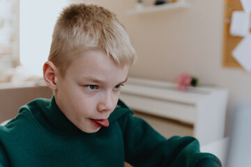 A boy with hearing aids focuses intently while playing a game on his laptop, showcasing modern...
