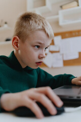 A boy with hearing aids focuses intently while playing a game on his laptop, showcasing modern...