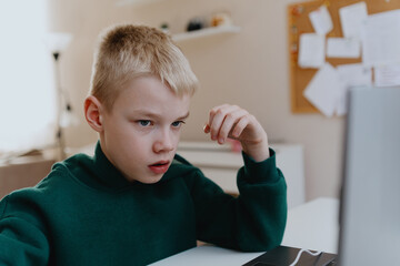 A boy with hearing aids focuses intently while playing a game on his laptop, showcasing modern...