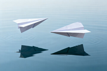 Two white paper airplanes floating on water with reflections and ripples