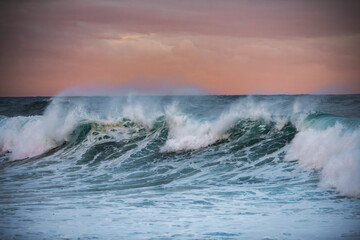 A powerful ocean wave rises under a soft pink and purple sunset sky at Bronte Beach, Sydney, Australia.