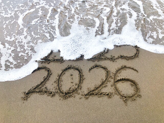 Year 2025 replaced by 2026 text written on beach sand. 2026 happy New Year coming concept. 
