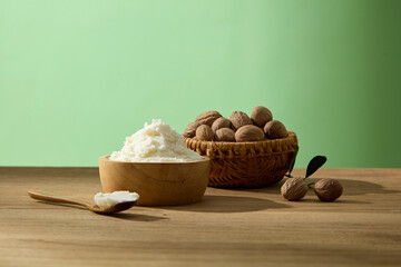 Bowl of shea butter styled with shea nuts and leaves. Presented in warm natural light on a wooden background. Front view, minimal scene for advertising