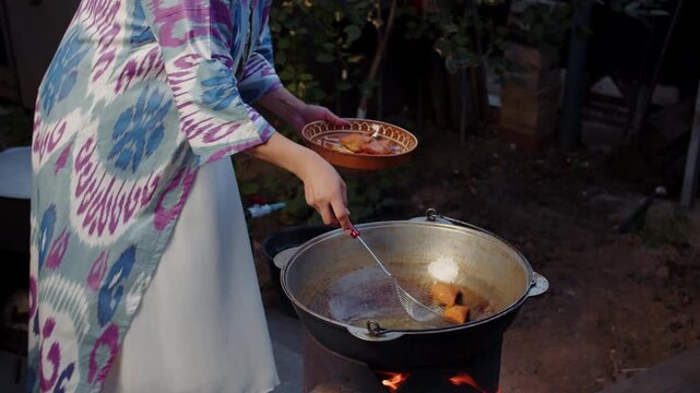 Woman taking fried baursak dough pieces from kazan cauldron outdoors