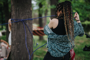 A young woman with braided hair attaches a hammock between trees in a scenic park, enjoying a peaceful, outdoor activity surrounded by greenery.