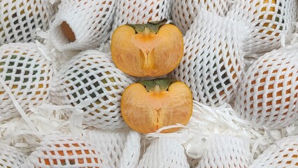 A vibrant display of persimmons wrapped in protective mesh, showcasing their bright orange color...
